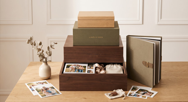 Trois boîtes à photos empilées sur une table de bois, le tiroir du bas ouvert sur des tirages rangés, un album relié posé à côté.